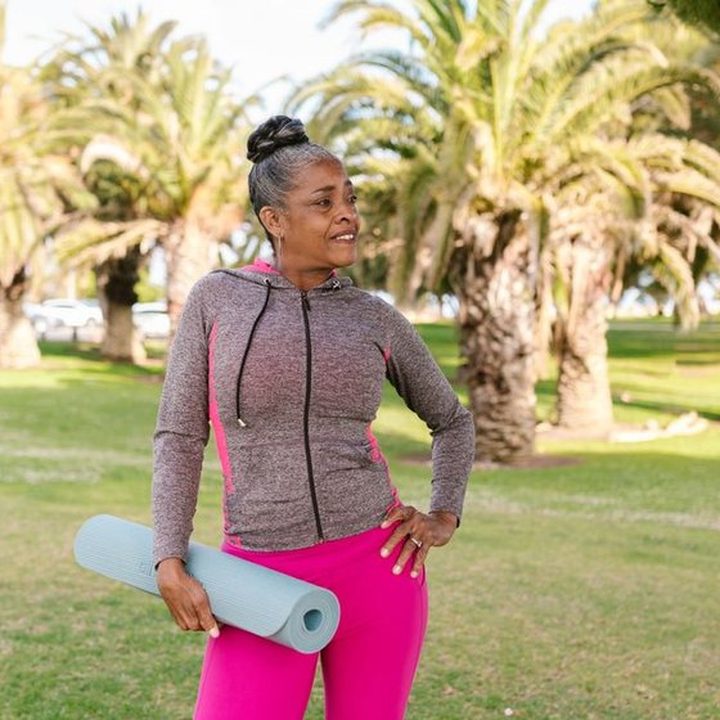 A woman carrying a yoga mat across a sunlit park